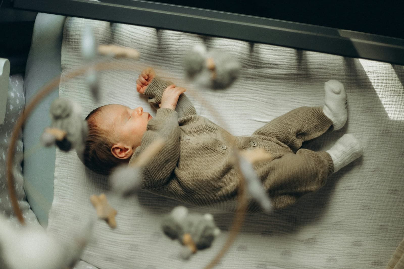 Un bébé endormi paisiblement dans son berceau, sous un mobile en bois
